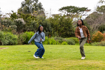 Two African American teenage females running across park lawn in knit sweater and white sneakers