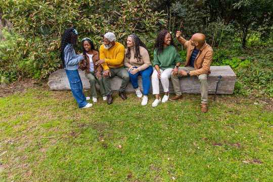 African American family chatting on carved wooden bench in park wearing fall clothing, cane visible