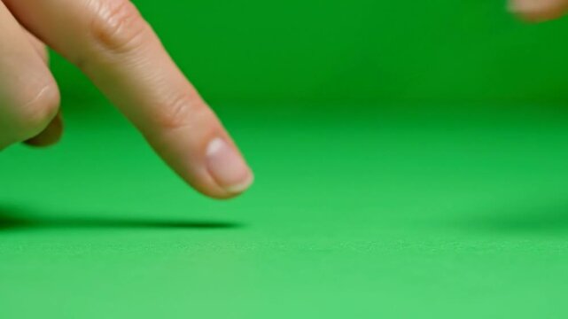Close-up of a human finger pointing down onto a vibrant green screen surface, with another finger partially visible.