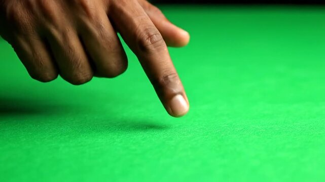 Close-up shot of a person's finger pointing down onto a vibrant green felt surface, possibly a billiard table.