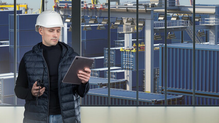 Fototapeta premium Port logistics, container terminal operations. Engineer in hard hat checks cargo data on tablet while overseeing stacked shipping containers and crane equipment.