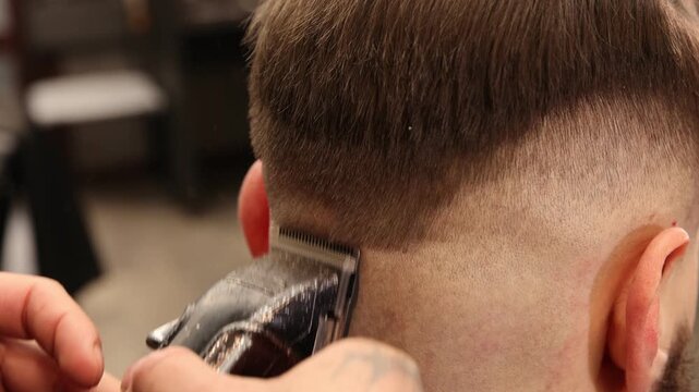 Stylist cutting man's hair with clipper in barbershop, closeup