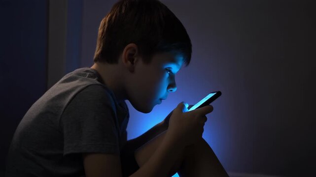 Young Boy Using Smartphone in Dark Room with Blue Light Reflection