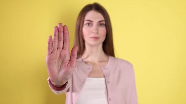 Woman making stop gesture on yellow background