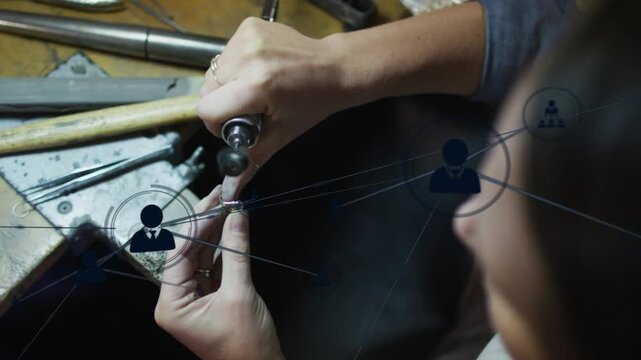 Jeweler turning Dremel and holding piece, polishing while blue network icons spreading over hands
