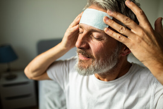 Mature man applying cooling forehead patch at home