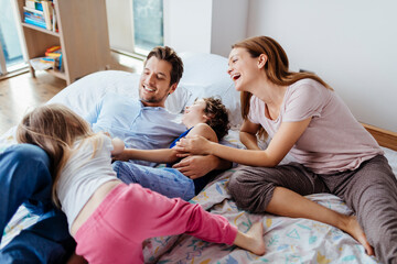 Obraz premium Parents and kids laughing and playing on bed at home