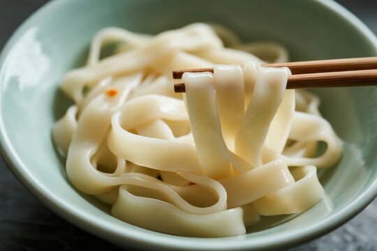 Close-up of wide rice noodles in a bowl being lifted with chopsticks