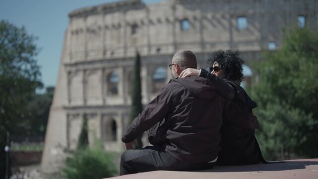 Curly hair woman and men with glasses couple shot positive vibes rising hands and having a party time at Parco Celio park look at Coloseum ancient arena during sightseeing tour in Rome