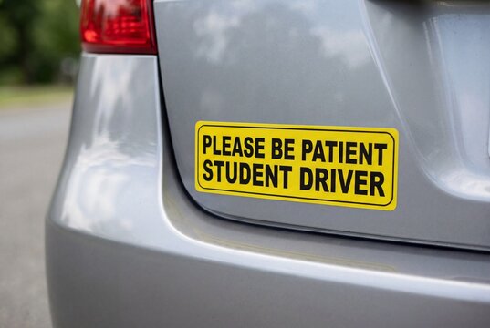 Yellow student driver bumper sticker on rear of silver car