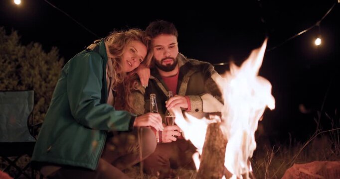 Friends enjoy a night by the fire while camping in nature under the stars with drinks and laughter in the mountains of Colorado