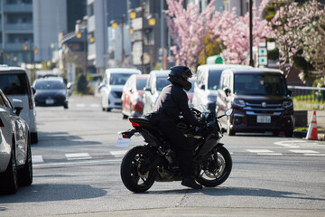 春の名城公園の路上で駐車する車の列とバイクを乗る若い男性の姿