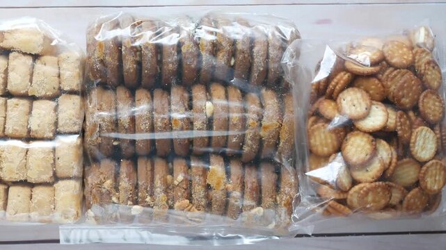 Top view of three different plastic bags with crispy cookies and crackers on wooden surface