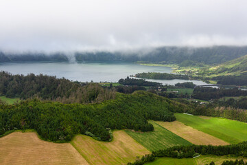 Fototapeta premium Sete Cidades, San Miguel Island, Azores, Portugal. Calm lake surrounded by lush forests. Cloudy sky and fog over the volcanic landscape.