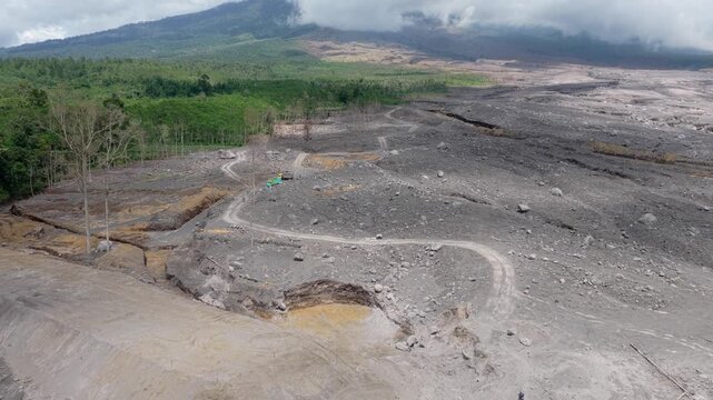 Aerial view showing the stark contrast between the lush green forest and the barren, ash covered land devastated by the semeru eruption