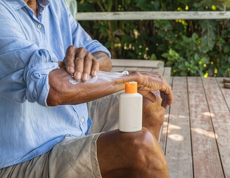 elderly man applying sunscreen on a hot day while sitting on his porch, could be used for messaging about heatwaves, SPF, sunscreen or skin cancer