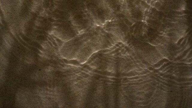 Tropical sunlight leaf shadow patterns moving on shallow water and sandy seabed abstract background