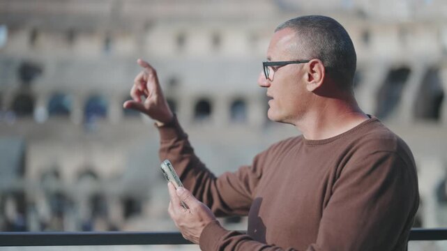 Young archaeologist checking reconstruction blueprint dimensions on phone compared with Colosseum present positions in Rome, Italy, slow motion cinematic isolated shot with selective focus