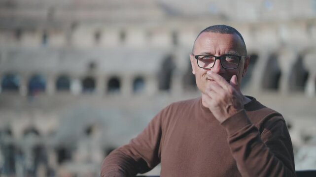 Portrait of young businessman looking at camera and smiling at visit of Colosseum in Rome. Slow motion cinematic shot with selective focus