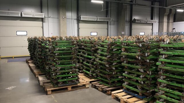 Massive stacks of green rolling dollies and transport bases in a large warehouse. Professional industrial equipment for heavy material handling, logistics movement and distribution center supply.