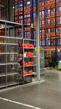 Modern industrial warehouse interior with orange safety helmets on shelves and empty racking systems. Concept of workplace security, personal protective equipment and organized logistics facility.