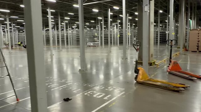 Pair of manual pallet jacks on a clean concrete floor in a vast empty warehouse. Professional industrial storage facility with high-rise shelving units ready for logistics and distribution operations.