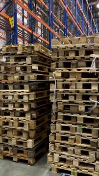 Stacked wooden euro pallets in a large modern warehouse. Industrial storage facility with blue racking systems for efficient logistics, pallet management and global supply chain operations.
