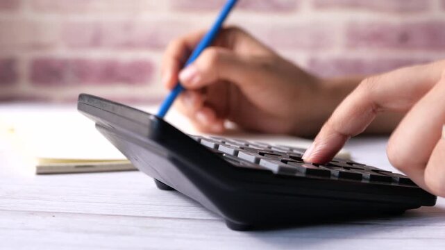 Person using calculator and writing on notebook for finance and business tasks