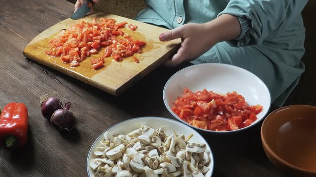 A woman's hands slice red tomatoes with a knife on a cutting board on the table
