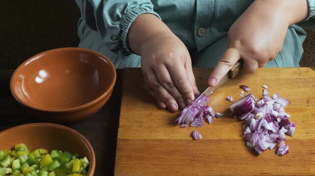 Hands chop red onions with a knife on a cutting board on the table