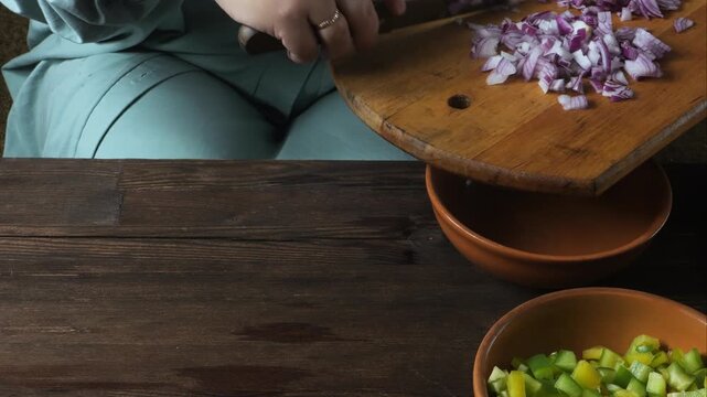 Hands chop red onions with a knife on a cutting board on the table