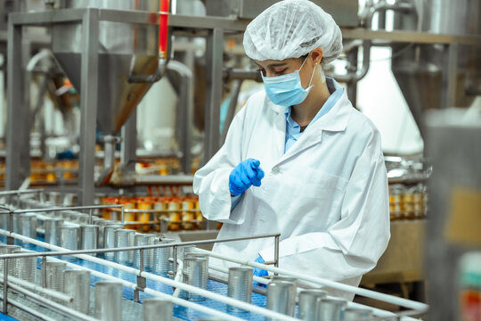 Food safety inspector observe canned seafood samples on production line while holding checklist inside regulated processing plant, ensuring HACCP compliance and contamination prevention standards.