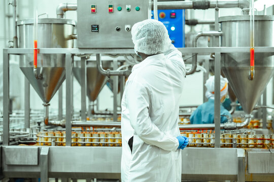 Food factory supervisor monitors automated sauce filling machine above canned seafood production line, checking control panel and ensuring hygiene compliance in regulated manufacturing environment.