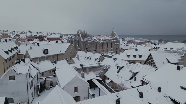 Drone Pullback from St Karins Ruin Over Snow Covered Rooftops in Visby, Gotland Sweden