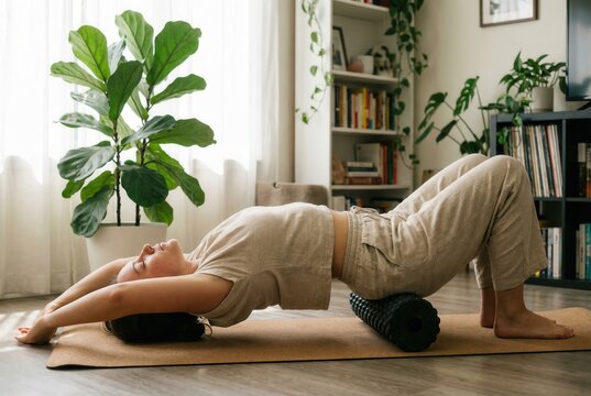 Woman performing upper back extension on foam roller at home