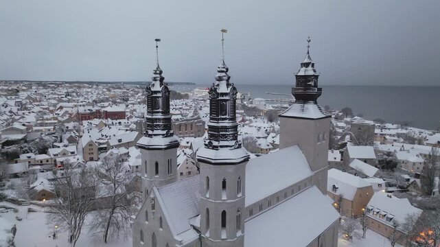 Aerial Orbit of Snow Covered Visby Cathedral Towers Above Visby Old Town in Winter, Gotland Sweden