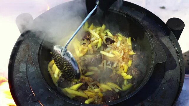Steam rising from frying pan with beef meat and potato, carrot placed on metal stove outdoors. Wilderness cuisine concept, expedition lifestyle and seasonal mood.