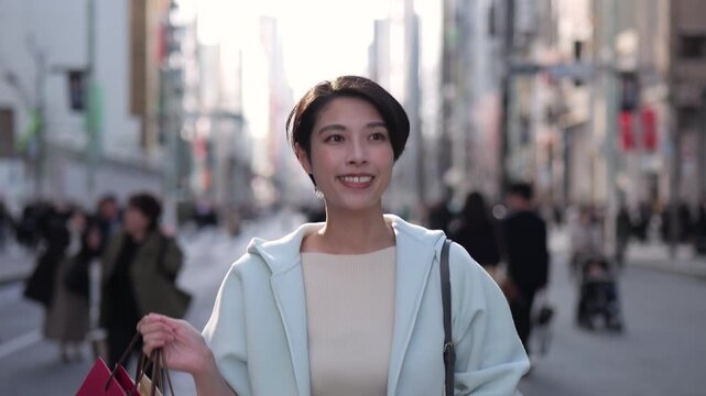 ショッピングバッグを持って銀座の通りを楽しそうに歩く女性のトラッキングショット