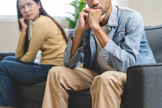Family problem concept. Tension in relationship between married couple, husband and wife staying sitting separate after quarrel in the living room.