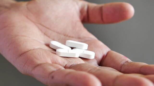 A close up view of an open palm holding four white oval shaped pills, shot from a high angle, motion footage