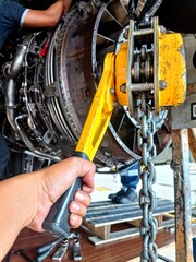 Fototapeta premium Close-up of an aircraft mechanic operating a manual chain hoist during jet engine maintenance inside an aircraft hangar