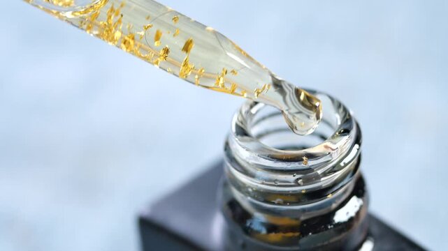 Liquid gold serum drips from pipette into cosmetic bottle for luxury skincare treatment