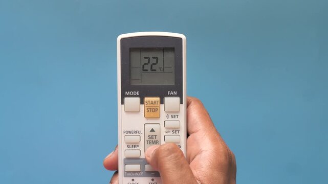Close-up shot of male hand using air conditioner remote control to adjust temperature, setting it lower for cooler air in a room