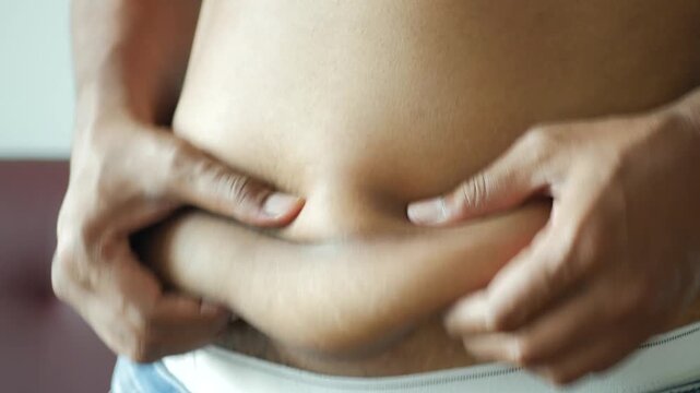 Close up hands touching stomach fat on body, showing health problems and excess weight, with copy space