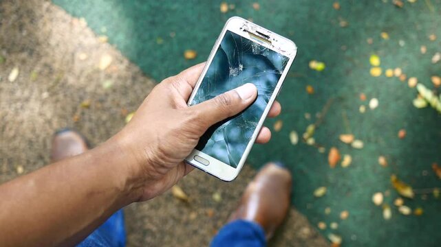 Top view of man holding white smartphone with broken screen outdoors