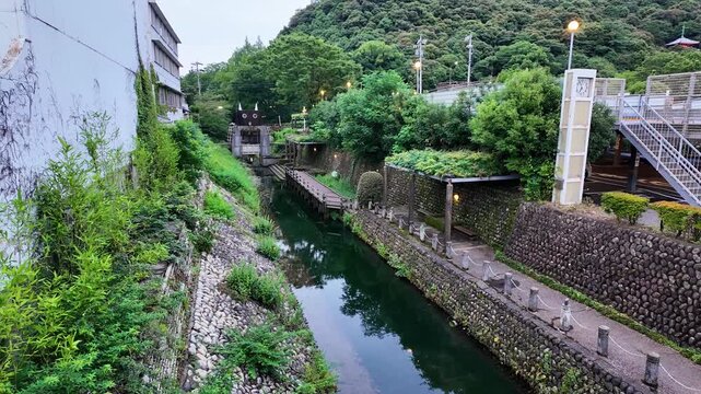 Urban drainage channel with a small sluice gate and pedestrian walkway in a Japanese neighborhood, designed for flood control and rainwater management with stone-walled embankments. Gifu, Japan
