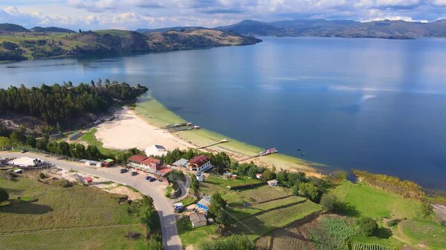 Stunning aerial shot of Tota Lagoon, showcasing lush green hills and tranquil blue waters under a cloudy sky.