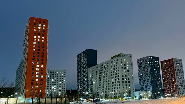 Modern colorful high-rise apartment buildings of Salaryevo Park residential complex in Moscow at dusk. Urban architecture with vibrant orange, green and grey facades under evening sky.