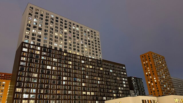 Modern colorful high-rise apartment buildings of Salaryevo Park residential complex in Moscow at dusk. Urban architecture with vibrant orange, green and grey facades under evening sky.