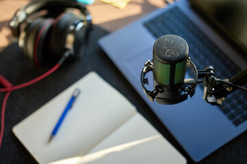 Fototapeta premium Close up of podcast microphone above laptop, headphones, and notebook on desk. Concept of recording, streaming and content creation